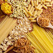 A spoonful of Barilla Tri-Color Rotini Pasta on a wooden surface with various types of pasta.