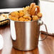 A mini stainless steel pail filled with fried onion rings and fries.