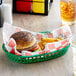A green plastic food basket lined with red check deli sandwich wrap paper, holding a hamburger and crinkle-cut fries.