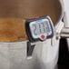 A digital probe thermometer with an adjustable head clipped to the side of a pot.