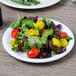 A Carlisle white melamine salad plate with salad on a table.