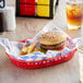 A red plastic food basket lined with blue check deli sandwich wrap paper, holding a hamburger and potato wedges.