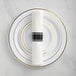A white plastic plate with gold and black bands set with rolled gold flatware on a white background.