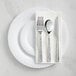 A white plastic plate with silver hammered flatware on it.