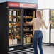 A woman standing in front of an Avantco wine merchandiser with bottles of wine.