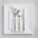 A white plastic plate with hammered silver plastic flatware on it.