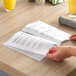 A person opening a H. Risch, Inc. clear menu cover on a table.