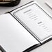 A black H. Risch, Inc. elastic band holding a menu on a white table.
