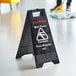 A black Lavex caution wet floor sign on a white floor.