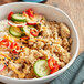 A bowl of rice and vegetables with a cucumber on the side.