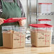 A person in an apron holding a red lid over a couple of Carlisle clear food storage containers.