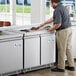 An Avantco stainless steel refrigerated salad bar on a counter in a commercial kitchen with a man preparing food.