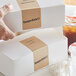 A hand using a TamperSafe Kraft Paper label to seal a box of food.