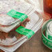 Plastic containers of food with green TamperSafe labels on a table.