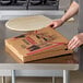 A person opening a Choice kraft corrugated pizza box on a table.