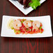 A rectangular white porcelain plate with shrimp and vegetables.