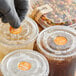 A gloved hand putting a TamperSafe orange label on a plastic cup of brown liquid.