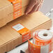 A person's hand uses a TamperSafe orange paper label on a box.