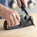 A hand using a Wusthof 2-stage knife sharpener to sharpen a knife.