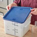 A woman opening a Choice white square plastic food storage container with a blue lid.