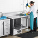 A man in a blue apron washing dishes on a stainless steel Regency dishtable in a commercial kitchen.