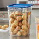 A Vigor clear square food storage container with a blue lid full of potatoes on a counter.