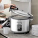 A woman using an Avantco commercial rice cooker to prepare food in a professional kitchen.