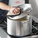 A person using a Choice aluminum sauce pot and lid to cook.