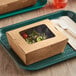 A salad in a Choice Kraft paper take-out container with a window on a table.