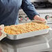 A woman using Choice aluminum baking and roasting pan with handles to serve food on a table.