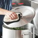 A hand using a pot holder to remove a lid from a pot.