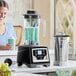 A commercial blender with a digital touchpad control, shown with both a clear plastic jar and a stainless steel jar.