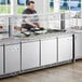 A man preparing food in an Avantco stainless steel refrigerated salad bar.