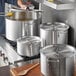 A man cooking in a professional kitchen with a Choice aluminum sauce pot on a stove.