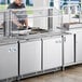 A man preparing food in a commercial kitchen using an Avantco stainless steel refrigerated salad bar.