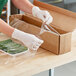 A hand using Western Plastics shrink wrap to cover a box of vegetables.