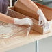 A person wearing gloves using Western Plastics perforated shrink wrap to cover a pizza.