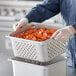 A person holding a Vigor stainless steel hotel pan full of cut carrots.