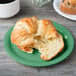 A croissant on a green Diamond Mardi Gras melamine plate next to a cup of coffee.