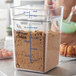 A person holding a clear Carlisle food storage container with a cake inside.