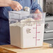 A person pouring flour into a Carlisle clear food storage container.