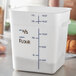 A close-up of a white Carlisle square food storage container with black writing on it.