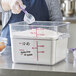 A person pouring flour from a measuring cup into a Carlisle clear polycarbonate food storage container.