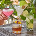 A hand holding an Acopa Endure plastic rocks glass filled with a pink drink and fruit.