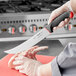 A person in gloves using a Schraf Cimeter knife to cut meat on a cutting board.