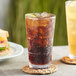 Two Acopa Tritan plastic pint glasses filled with soda on a table with a sandwich.