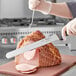 A person slicing a large piece of ham with a Schraf serrated knife.