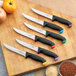 A Schraf serrated utility knife with a blue handle in a group of knives with black handles.