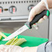 A gloved hand uses a Schraf serrated utility knife with a green handle to cut celery on a cutting board.