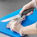 A person in gloves using a Schraf utility knife with a blue TPRgrip handle to cut fish on a blue cutting board.